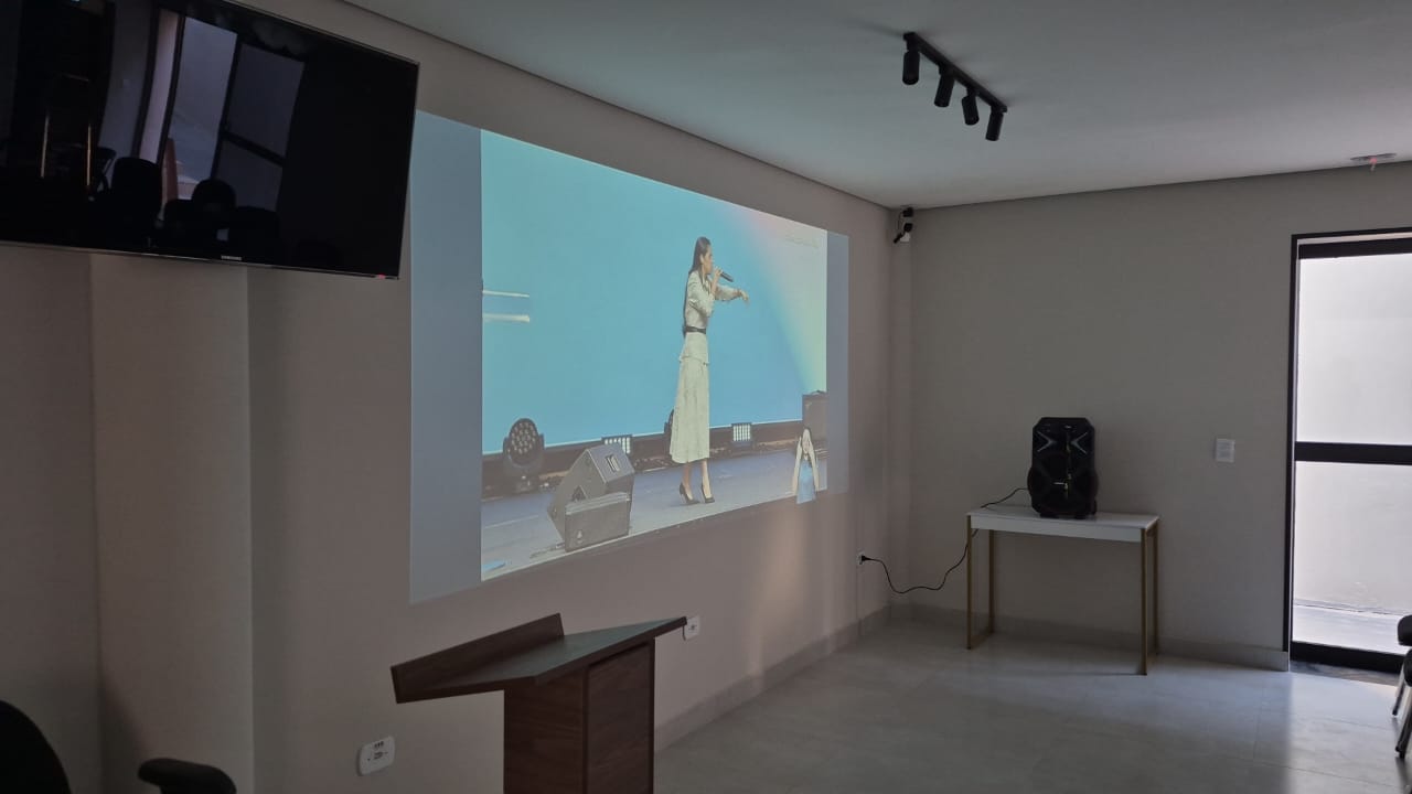 Projeção durante apresentação, com púlpito, som e portas de vidro fumê ao fundo.